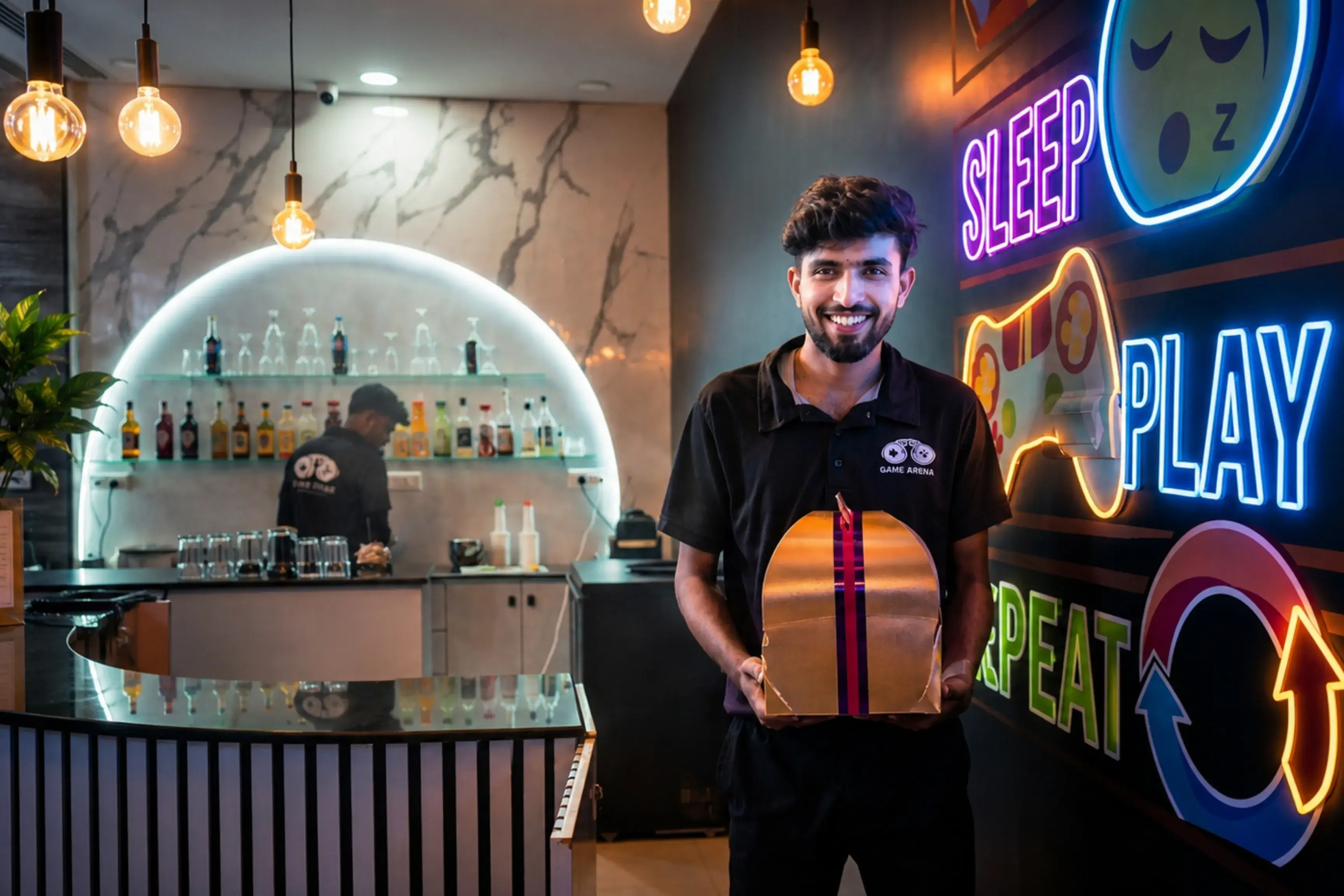 Game Xtreme staff member smiling and holding a birthday cake box in front of the neon Sleep Play Repeat sign