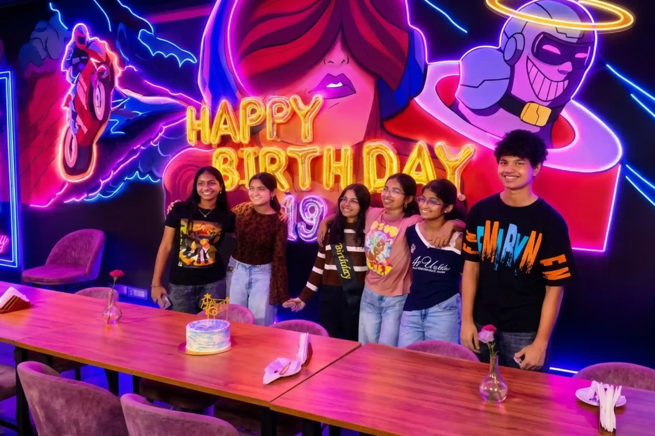 Group of six teenagers posing with HAPPY BIRTHDAY 19 foil balloons and birthday sash against neon mural