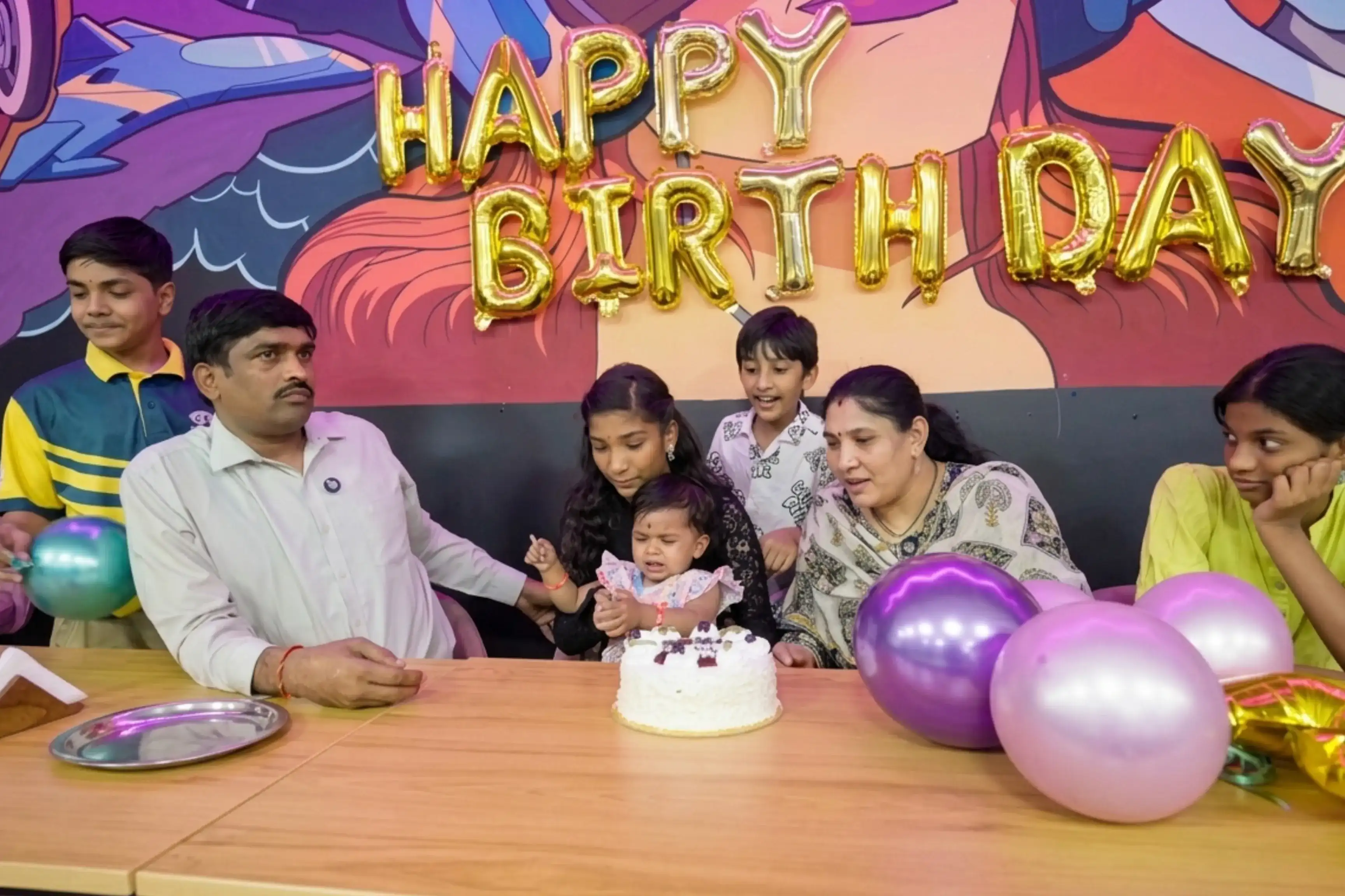 Family celebrating a baby's first birthday with cake and gold foil letters at Game Xtreme