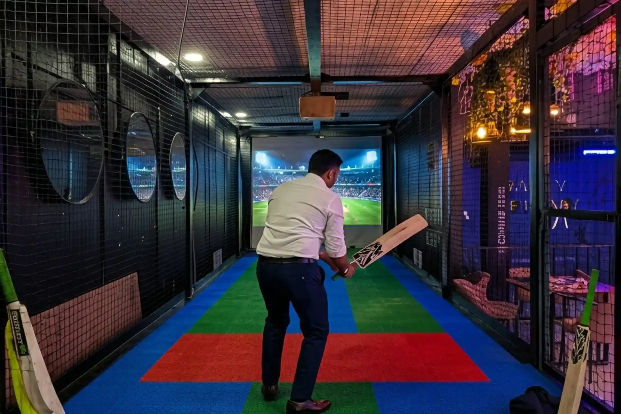 Man in batting position facing projected cricket stadium in indoor simulator at Game Xtreme